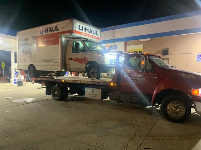 Box truck secured on a Major League flatbed at a lit fuel station at night