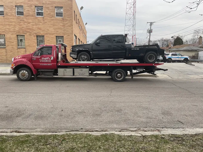 Major League flatbed carrying a black pickup truck down a South Side residential street
