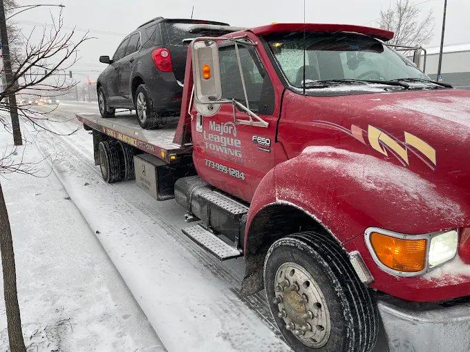 Flatbed hauling an SUV through heavy snow on a Chicago roadway